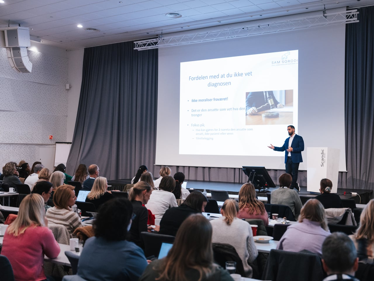 Sam Sorodi på scenen foran et stort publikum på konferanse